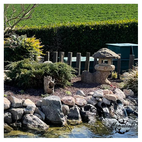 Lanterne Yamatoro grès installée en berge de bassin naturel avec enrochement et plantations chantier MonBassin